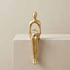 Gold sculpture of a seated figure on a beige surface