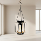 Black lantern with clear glass shade hanging in a room with light-colored walls and windows.