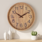 Wooden wall clock on a wall with decorative vases and a cactus plant below.