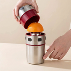 Person using a portable orange juicer with a red top and silver body on a beige background