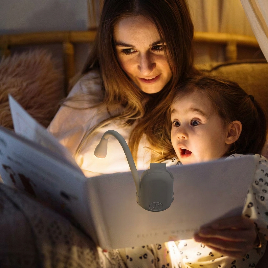 Woman and child reading a book with a lamp attached, in a cozy indoor setting.