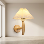 Wooden wall sconce with pleated lampshade on a neutral wall.