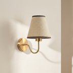 Wall-mounted lamp with a beige shade and gold fixture on a light beige wall.