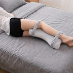 Person lying on a bed wearing gray knee-high socks with white tops.