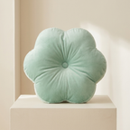 Mint green flower-shaped pillow on a beige surface with a neutral background