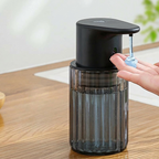 Black and transparent soap dispenser on a wooden surface with a hand reaching out to dispense soap.