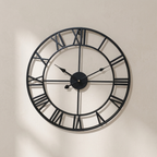 Large black wall clock with Roman numerals on a beige wall