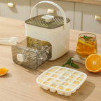 Ice cube tray with lid, ice cubes, and a glass of iced tea on a wooden surface.
