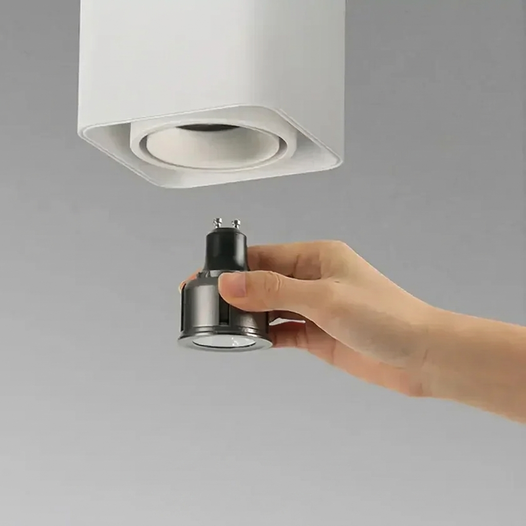 Hand holding a light bulb adapter near a ceiling light fixture on a gray background
