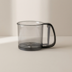 A translucent smoky gray plastic container with a matching dark gray handle and base, shown on a clean, light beige studio background.