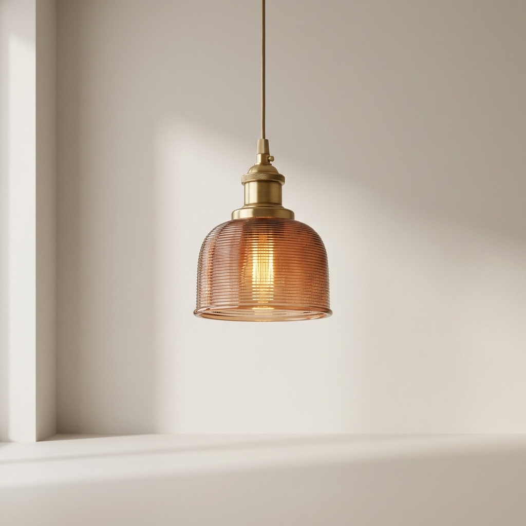 A hanging pendant light with a ribbed amber glass dome shade and brass-toned metal hardware, suspended against a warm off-white wall.