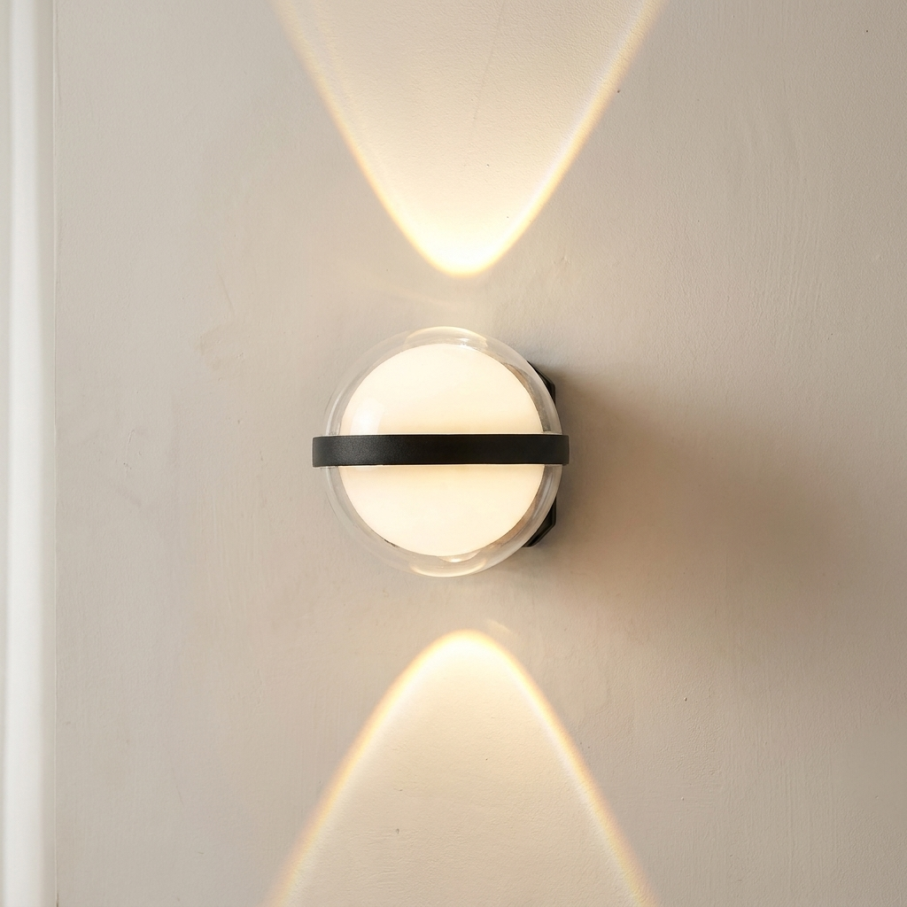 A modern spherical wall sconce light fixture with a black horizontal band and clear glass cover, mounted on a beige wall and casting a warm upward light beam.