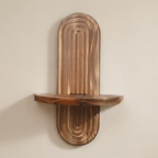 A rustic wooden wall shelf with a unique arched, ribbed backplate and a curved horizontal shelf, mounted on a plain beige wall.