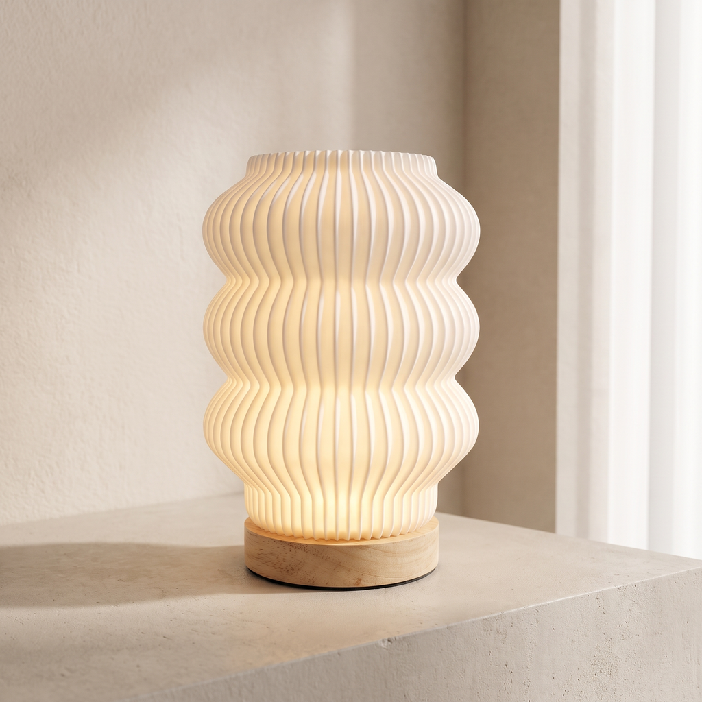 A modern ribbed table lamp with a warm glowing white pleated shade and a light natural wood base, styled on a concrete ledge against a neutral beige wall.