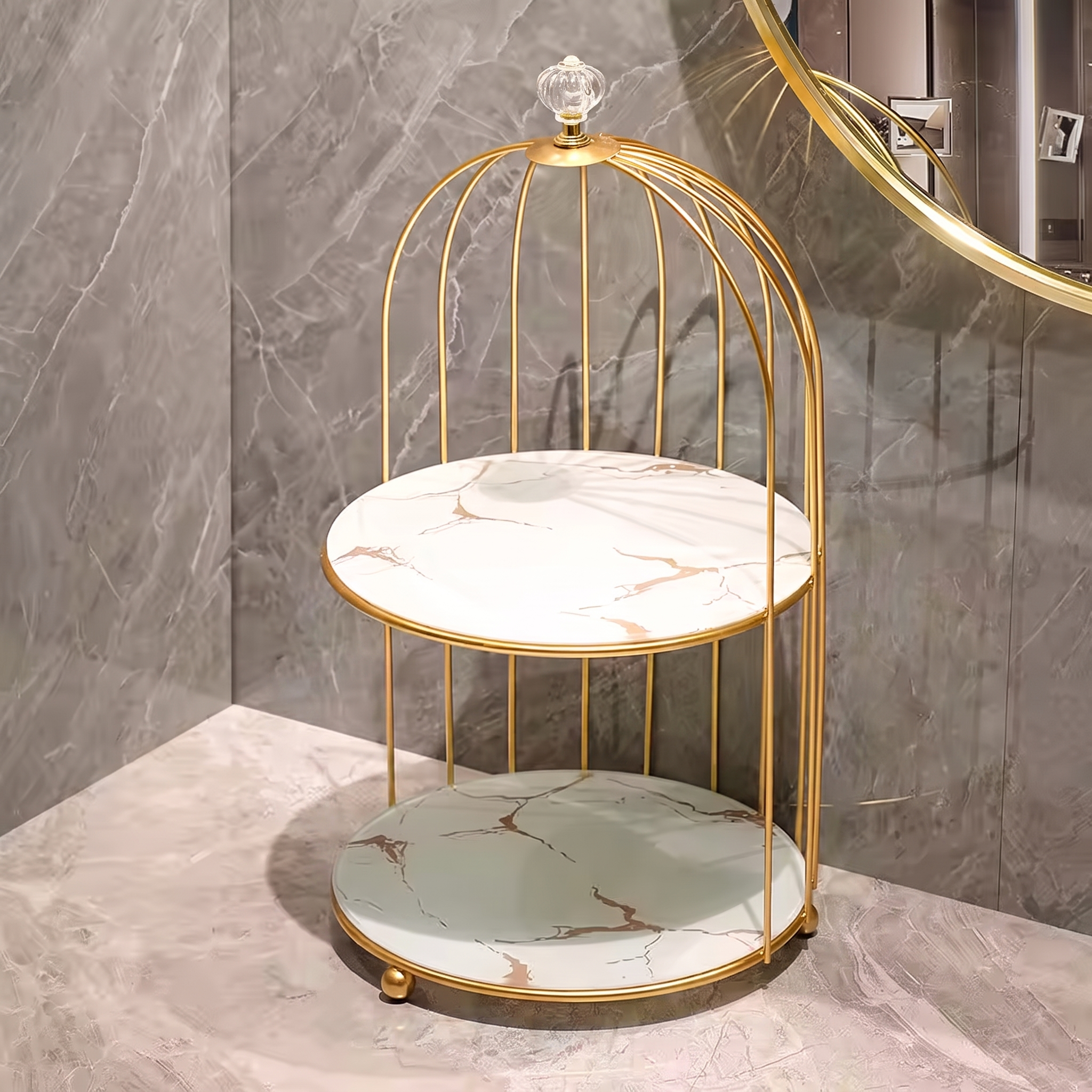 A two-tier decorative side table with a gold metal birdcage frame and marble-patterned plates, set on a marble surface against a gray marble wall.