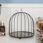 A black metal birdcage-style decorative stand with a round marble-patterned base and a clear crystal finial on top, displayed on a tabletop next to a Estee Lauder bottle and dried flowers.