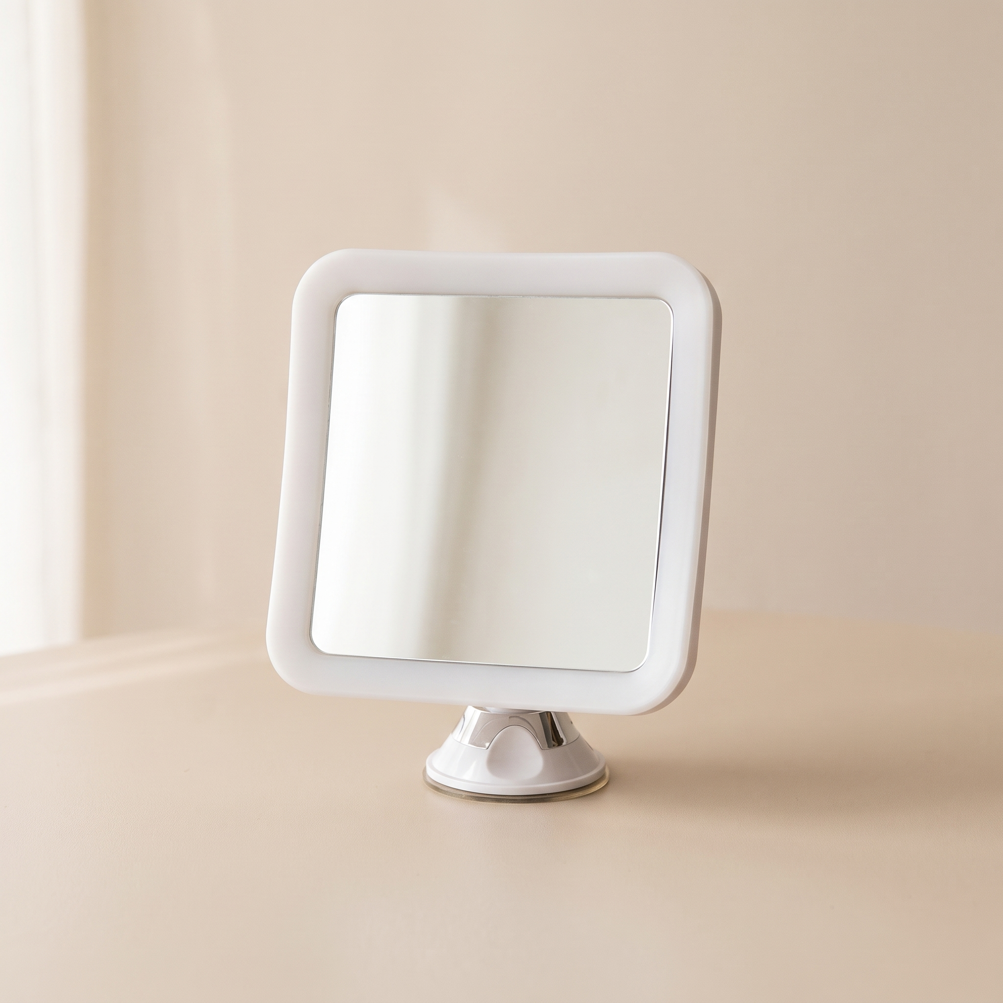 A square vanity mirror with a white frame and a silver stand, set against a soft beige background.