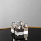 A clear glass or acrylic square ashtray with a reflective, polished finish, standing on a black reflective surface against a light gray background.