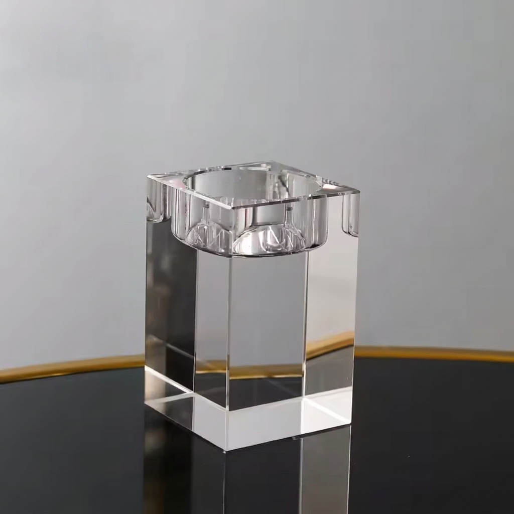 A clear acrylic or glass rectangular block with a square top, photographed on a dark reflective surface against a light gray background.