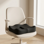 A black contoured lumbar support seat cushion placed on a cream-colored office chair in a bright, minimalist room with a window.