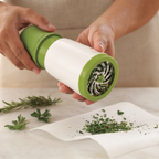 Green and white herb grinder with fresh herbs on a white surface