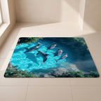 A rectangular floor mat with rounded corners lies on a light beige tiled floor in a sunlit room corner. The mat features a printed underwater scene with several dolphins swimming in bright turquoise water, dark blue water, rocks, and green seaweed.