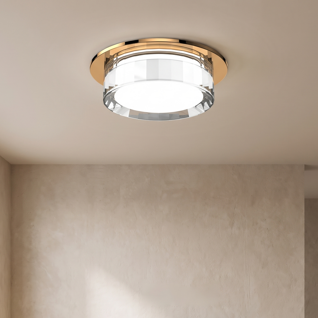 A modern semi-flush ceiling light fixture with a brushed gold metal frame and a clear glass shade, installed on a beige ceiling in a minimalist, neutral-toned living room.