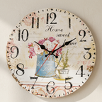 A round vintage-style wall clock with a distressed cream background, black distressed numerals, black hands, a red second hand, and a central floral and teacup illustration in pink, blue, and green tones.