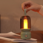 A hand holds a small lantern-style lamp with a glowing warm light inside a translucent smoky dome, resting on an open book in a softly lit indoor setting.