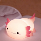 A cute axolotl-shaped night light glowing with warm pink and peach light, resting on a soft white surface.