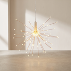 A hanging pendant light shaped like a burst of copper-colored wire with many small glowing bulbs, suspended from a white cord in a minimalist indoor setting.