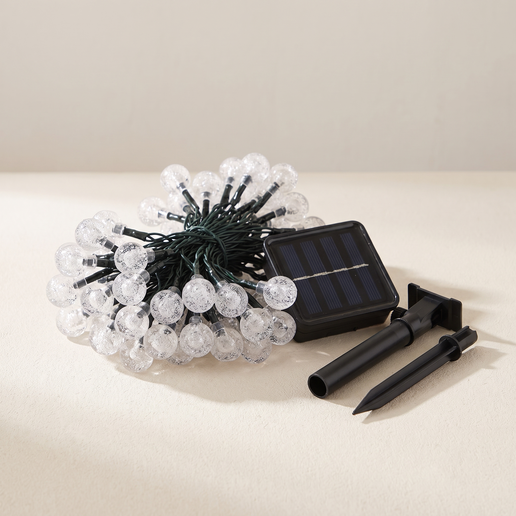 Solar string lights with clear faceted round bulbs, a small black solar panel, and two black ground stakes on a light beige surface.