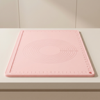 A pink silicone baking mat with embossed measurement markings and concentric circle guides, shown on a light beige countertop.