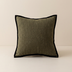 A square throw pillow with a textured olive green linen-like center and a contrasting black velvet piped border, set against a neutral cream background.