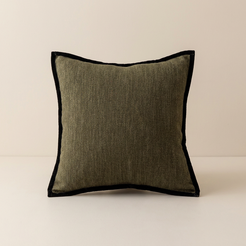 A square throw pillow with a textured olive green linen-like center and a contrasting black velvet piped border, set against a neutral cream background.