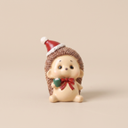 A small decorative hedgehog figurine with a cream-colored face and body, brown spiky texture, a red Santa hat, and a red bow with a green accent, standing against a plain beige background.