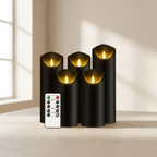 Four black flameless LED pillar candles with warm yellow glowing flames, arranged on a beige surface with a white remote control in front, set against a softly lit neutral interior background.