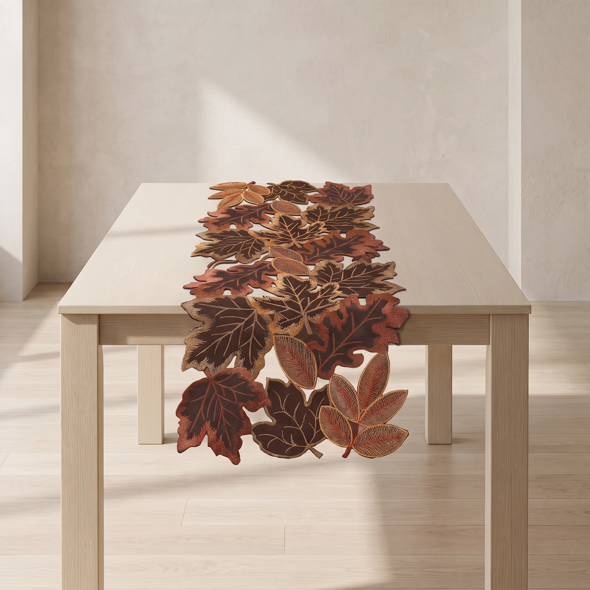 An autumn-themed table runner made of layered, realistic faux leaves in shades of brown, rust, and orange, displayed on a light wood dining table in a minimalist room.