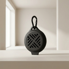 A round black portable speaker with a carabiner clip, standing on a white ledge in a minimalist, warm-toned interior setting.