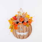 A burlap pumpkin Halloween wall hanging decorated with orange and yellow autumn flowers, leaves, pinecones, and a large burlap bow, shown against a plain white background.