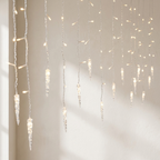 Iced candle-style string lights hanging in vertical strands against a plain light beige wall, casting a warm glow.