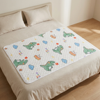 A quilted baby mattress protector with a colorful cartoon dinosaur and cloud pattern, shown on a bed with beige bedding in a brightly lit bedroom.