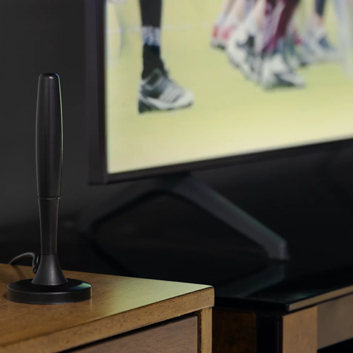Black TV antenna on a wooden surface with a blurred TV in the background