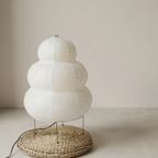 White paper lantern-style lamp with woven base on a neutral background