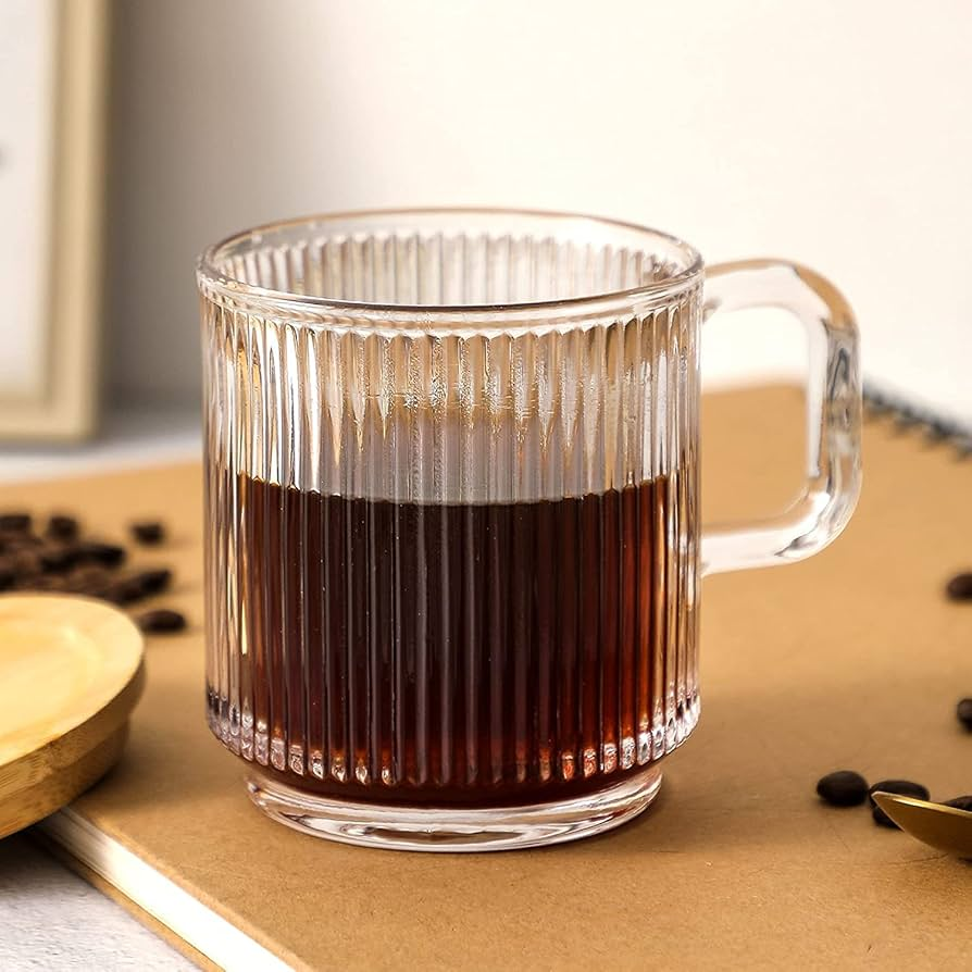 Clear glass mug with coffee on a wooden surface with coffee beans