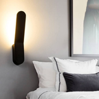 Modern wall lamp on a gray wall above a bed with white and gray bedding.