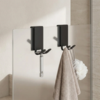 Black wall hooks with a towel and decorative item on a tiled wall.