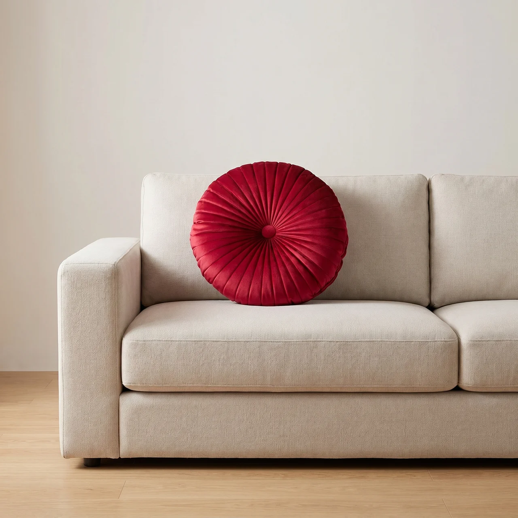 Beige sofa with a red round pillow against a plain wall