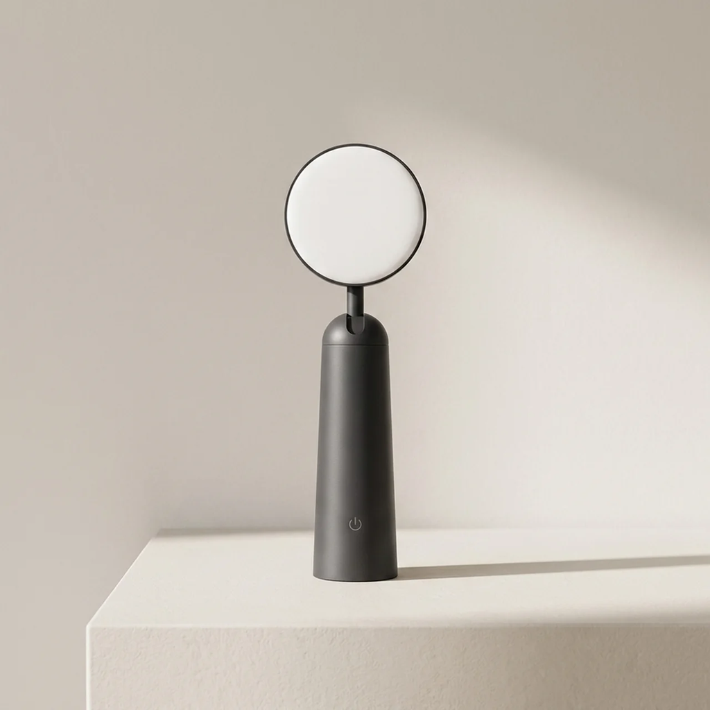 Black handheld mirror with round white surface on a beige background