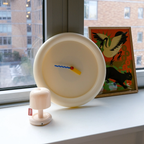 Round beige clock with colorful hands on a windowsill next to a framed picture